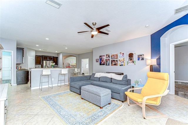 living area with visible vents, arched walkways, ceiling fan, and a textured ceiling