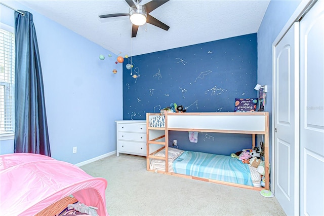 carpeted bedroom with a textured ceiling, an accent wall, a ceiling fan, and baseboards