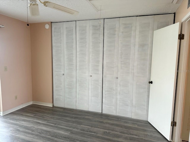 unfurnished bedroom featuring a textured ceiling, a closet, baseboards, and dark wood-type flooring