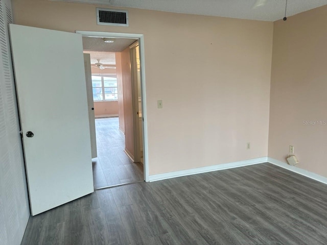 unfurnished room featuring dark wood-type flooring, a ceiling fan, visible vents, and baseboards