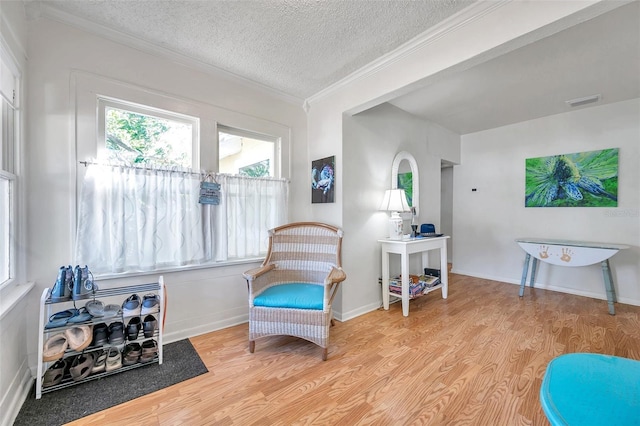 living area with baseboards, visible vents, light wood-style flooring, ornamental molding, and a textured ceiling