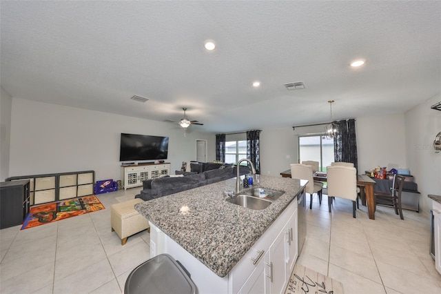 kitchen with light tile patterned floors, a kitchen island with sink, white cabinetry, and a sink