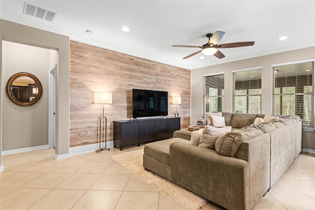 living area featuring light tile patterned floors, an accent wall, visible vents, and crown molding