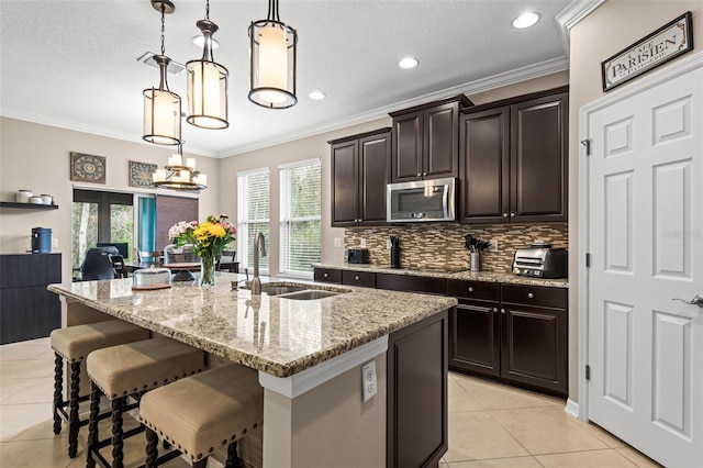 kitchen featuring an island with sink, stainless steel microwave, a sink, and decorative light fixtures