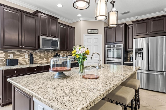 kitchen with a kitchen island with sink, a sink, visible vents, appliances with stainless steel finishes, and decorative light fixtures