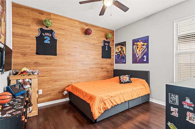 bedroom featuring wood walls, ceiling fan, baseboards, and dark wood-type flooring