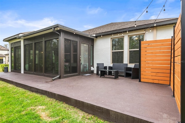 rear view of property with a sunroom, a shingled roof, a patio area, and stucco siding