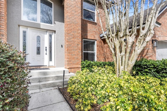 view of exterior entry featuring brick siding and stucco siding