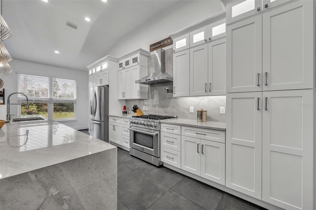 kitchen featuring stainless steel appliances, glass insert cabinets, white cabinetry, a sink, and wall chimney exhaust hood