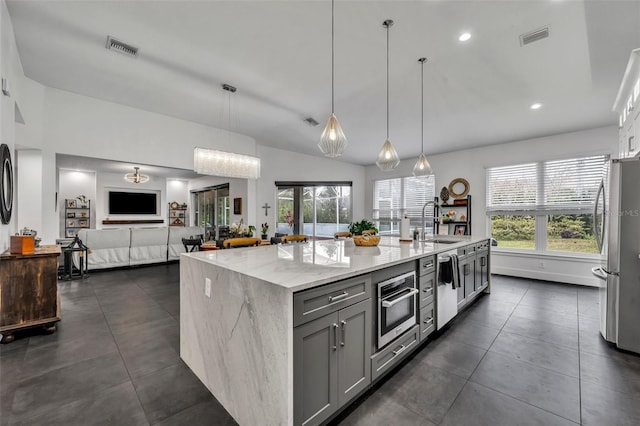 kitchen with appliances with stainless steel finishes, hanging light fixtures, light stone countertops, a kitchen island with sink, and gray cabinetry