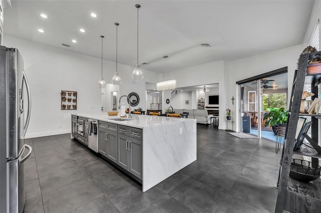 kitchen featuring open floor plan, freestanding refrigerator, a kitchen island with sink, gray cabinetry, and a sink