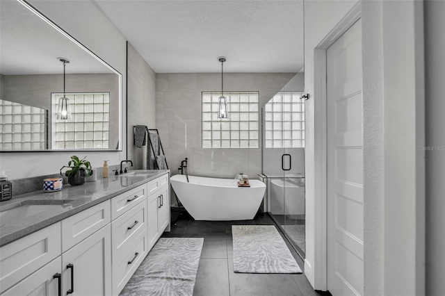 full bath featuring a stall shower, a sink, a textured ceiling, a freestanding tub, and tile walls