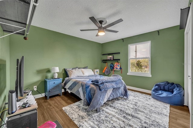 bedroom with a ceiling fan, a textured ceiling, baseboards, and wood finished floors