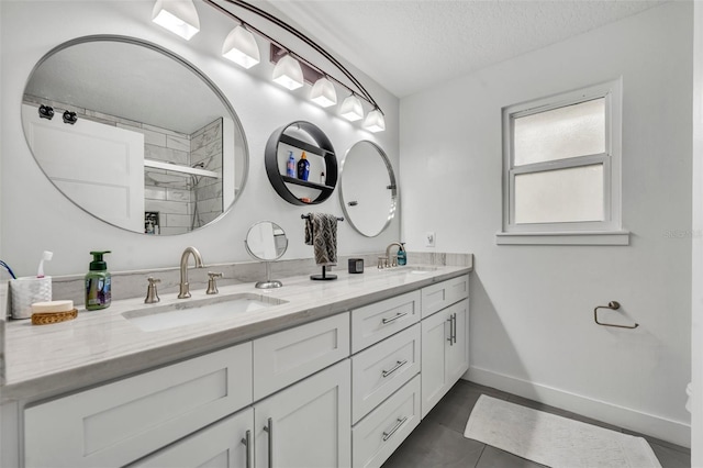 full bathroom with a textured ceiling, a sink, baseboards, tiled shower, and double vanity