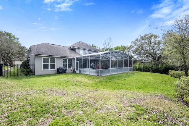 rear view of house featuring glass enclosure, a lawn, fence, and stucco siding