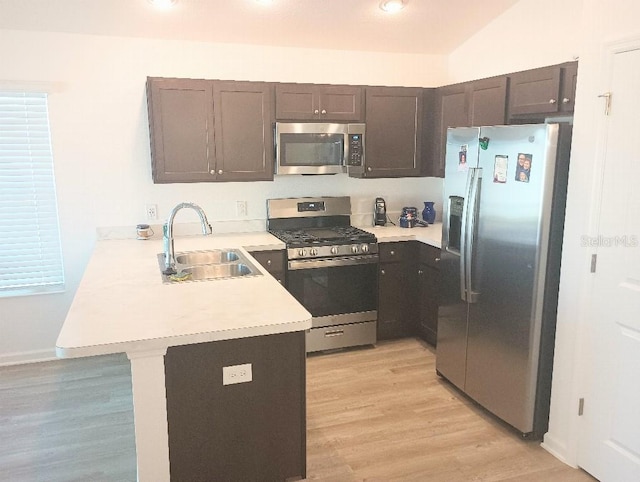 kitchen featuring stainless steel appliances, light countertops, a sink, light wood-type flooring, and a peninsula