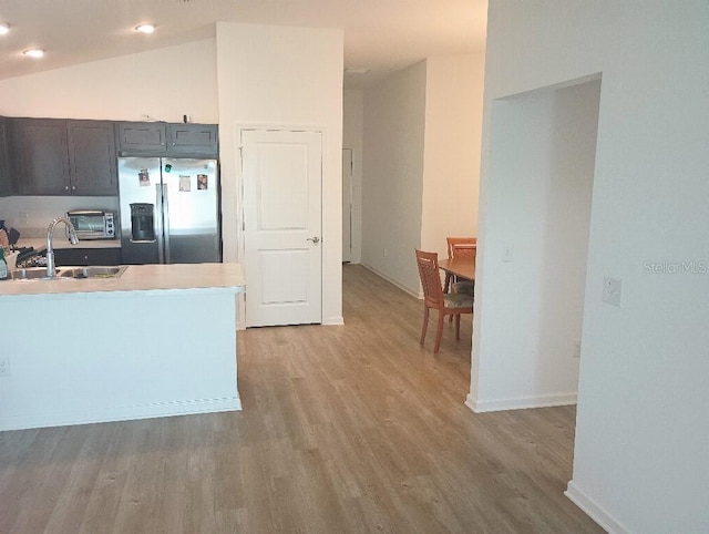 kitchen with light wood finished floors, vaulted ceiling, light countertops, stainless steel refrigerator with ice dispenser, and a sink