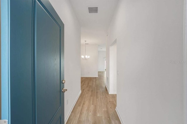 hall with a chandelier, light wood-type flooring, visible vents, and baseboards