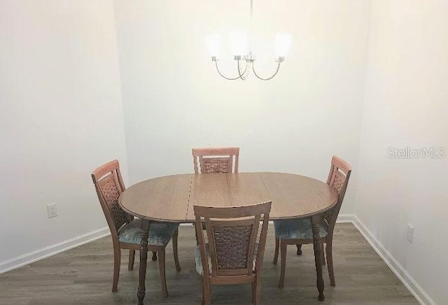 dining area with dark wood-type flooring, an inviting chandelier, and baseboards