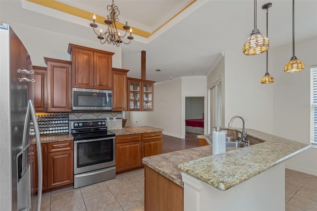 kitchen with a tray ceiling, brown cabinets, a center island with sink, stainless steel appliances, and glass insert cabinets