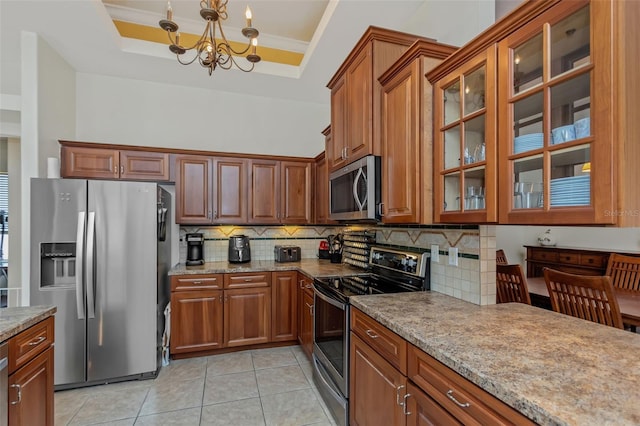 kitchen featuring stainless steel appliances, a raised ceiling, glass insert cabinets, and light stone countertops