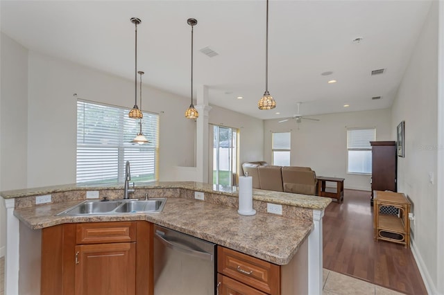 kitchen with brown cabinetry, open floor plan, a sink, pendant lighting, and stainless steel dishwasher