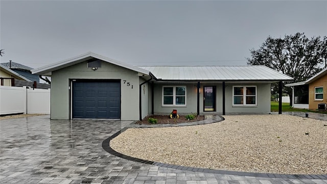 single story home with a garage, metal roof, fence, decorative driveway, and stucco siding