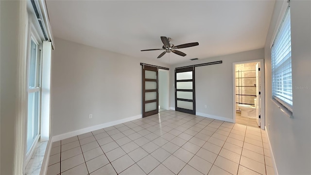 empty room with a barn door, light tile patterned flooring, visible vents, a ceiling fan, and baseboards