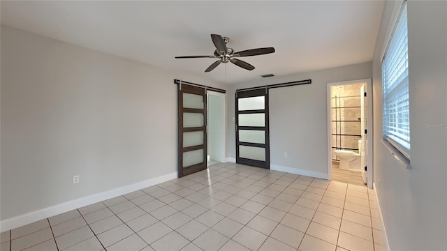 unfurnished room featuring a barn door, baseboards, visible vents, a ceiling fan, and light tile patterned flooring