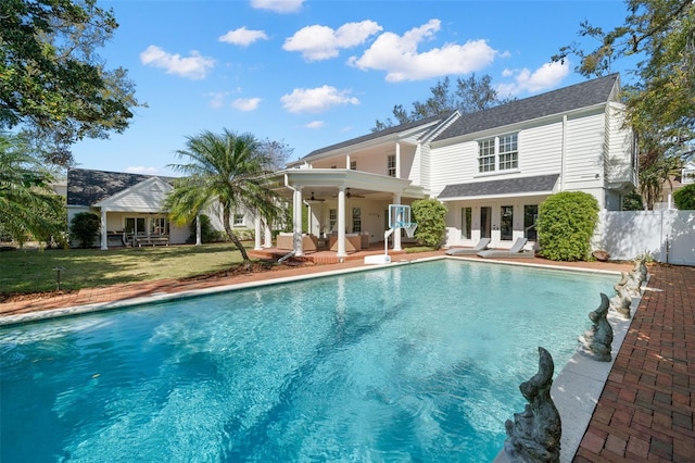 back of house with ceiling fan, fence, an outdoor pool, and a lawn