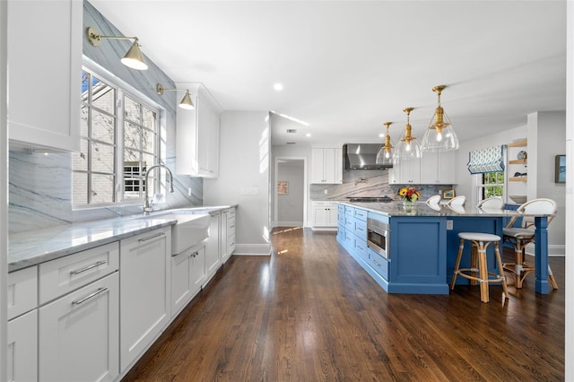 kitchen with stainless steel appliances, a sink, white cabinets, wall chimney range hood, and dark wood finished floors