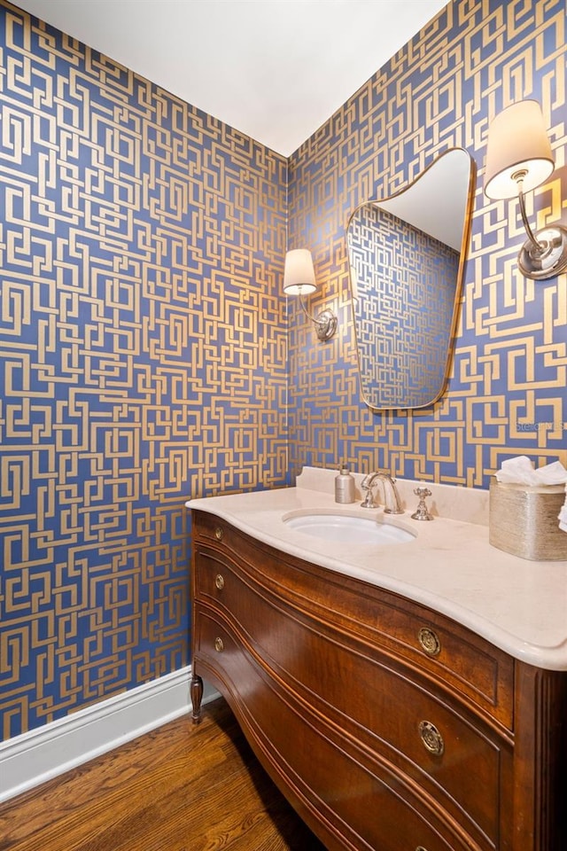 bathroom with baseboards, wood finished floors, vanity, and wallpapered walls