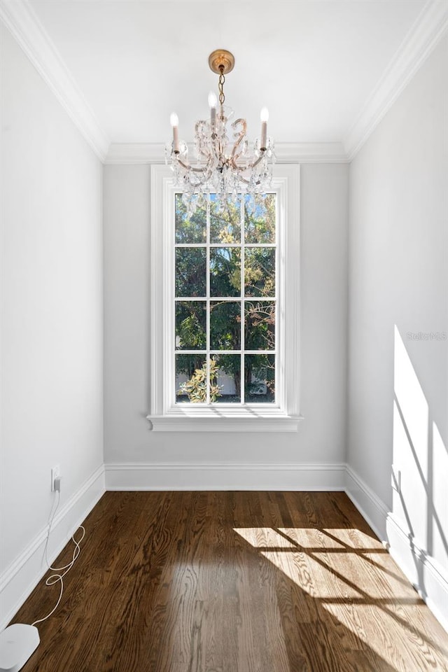 unfurnished dining area featuring a chandelier, crown molding, baseboards, and wood finished floors