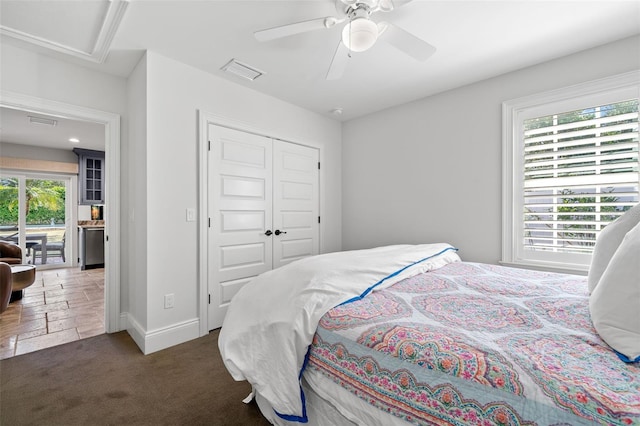 carpeted bedroom featuring a closet, stone tile flooring, visible vents, a ceiling fan, and baseboards