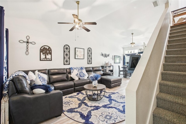 living room featuring light wood finished floors, visible vents, a high ceiling, ceiling fan, and stairs