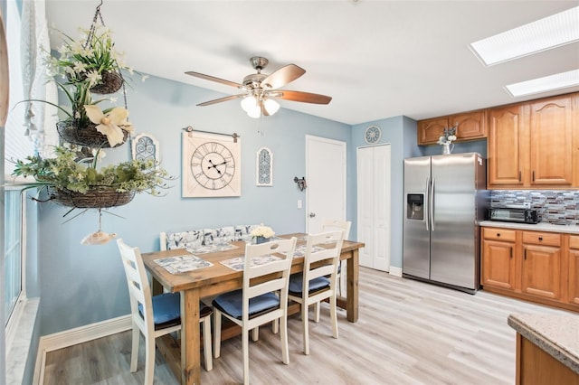 dining area with ceiling fan, a skylight, light wood-style flooring, and baseboards