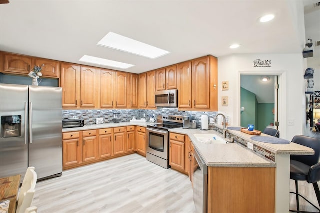 kitchen featuring stainless steel appliances, a peninsula, a sink, a kitchen breakfast bar, and decorative backsplash