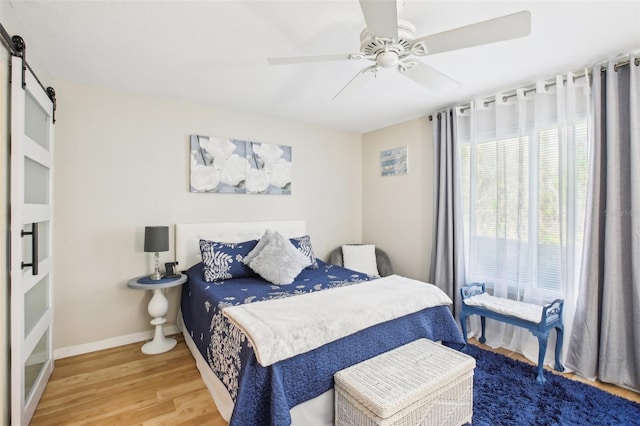 bedroom featuring ceiling fan, a barn door, wood finished floors, and baseboards