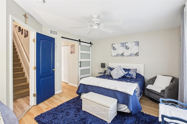 bedroom featuring a barn door, visible vents, baseboards, a ceiling fan, and light wood-type flooring