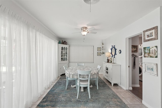 dining area featuring a ceiling fan, baseboards, light tile patterned flooring, and stacked washing maching and dryer