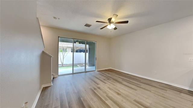 empty room featuring baseboards, visible vents, a ceiling fan, light wood-style flooring, and a textured ceiling