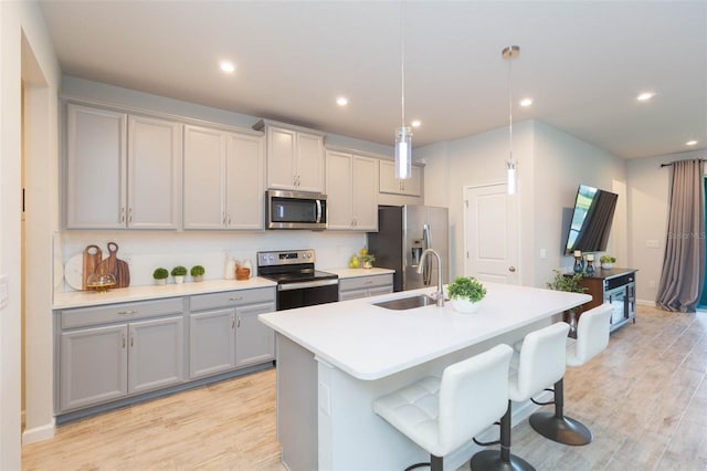 kitchen featuring light wood-style flooring, a sink, appliances with stainless steel finishes, gray cabinets, and an island with sink