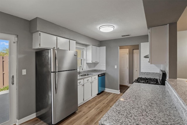 kitchen featuring gas range oven, visible vents, freestanding refrigerator, a sink, and dishwashing machine