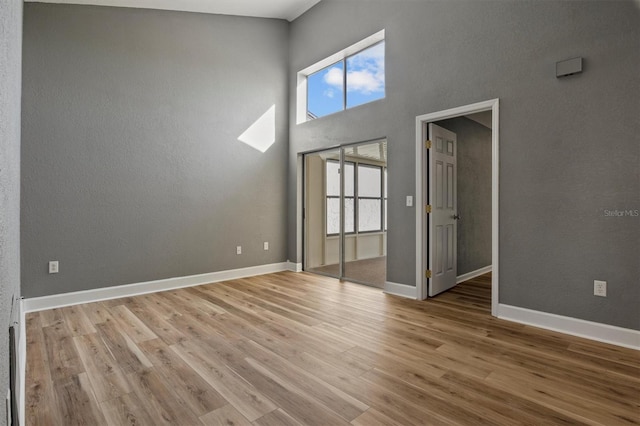 empty room with a high ceiling, baseboards, and wood finished floors