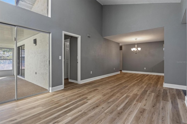 unfurnished living room featuring a towering ceiling, an inviting chandelier, baseboards, and wood finished floors