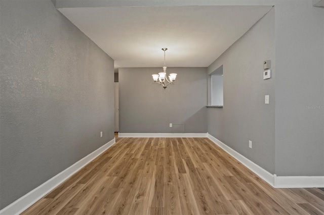 unfurnished dining area featuring light wood finished floors, an inviting chandelier, and baseboards