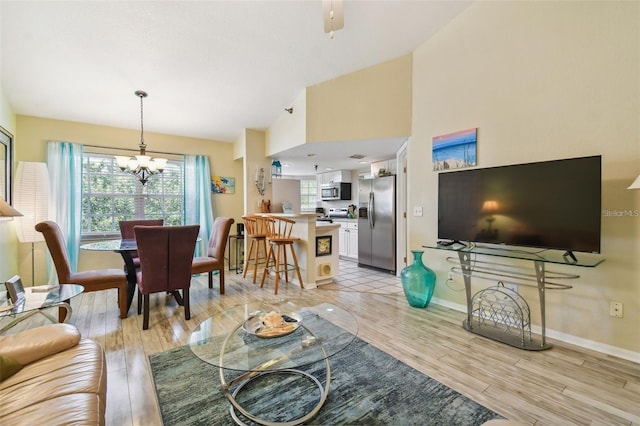 living area featuring a chandelier, light wood-type flooring, lofted ceiling, and baseboards