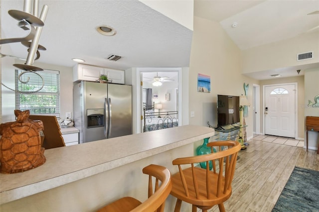 kitchen with light wood-style flooring, stainless steel fridge, vaulted ceiling, and visible vents