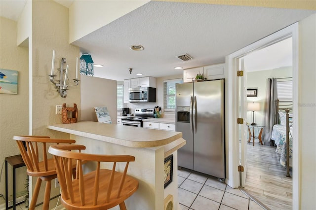 kitchen featuring visible vents, appliances with stainless steel finishes, a kitchen breakfast bar, a peninsula, and light countertops