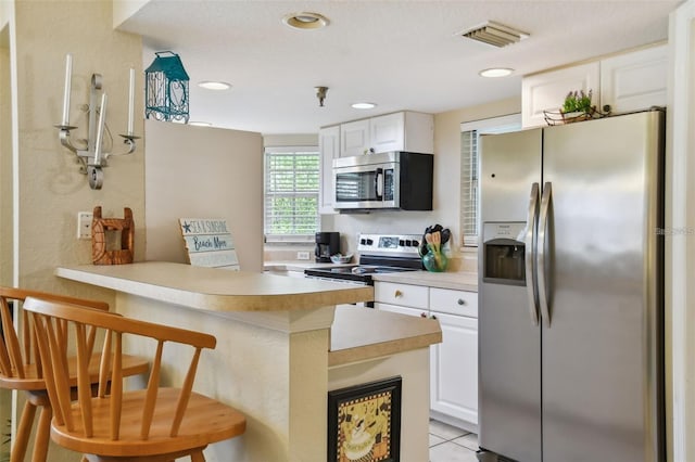 kitchen featuring stainless steel appliances, a peninsula, visible vents, white cabinetry, and light countertops